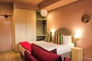 A hotel room with a bed, a wardrobe, a mirror, and a bedside table.