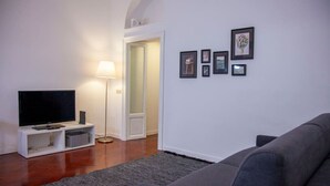 A living room with a flat-screen TV on a white stand, a grey sofa, a floor lamp, and a grey rug. - Navigli Beautiful Apartment in MILAN Near TRAM (Milano)