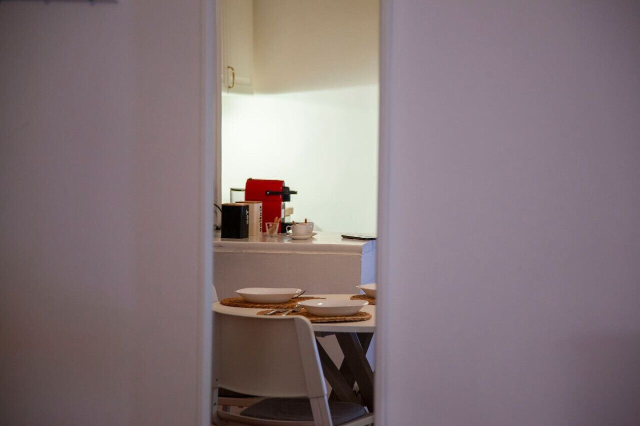 A small dining area with a white table set for two, a red appliance, and a white chair.