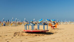 Een strand met rijen ligbedden en parasols, een schommel en een draaimolen.
