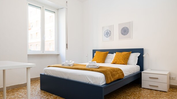 A bedroom with a bed, a bedside table, a nightstand, and a window.