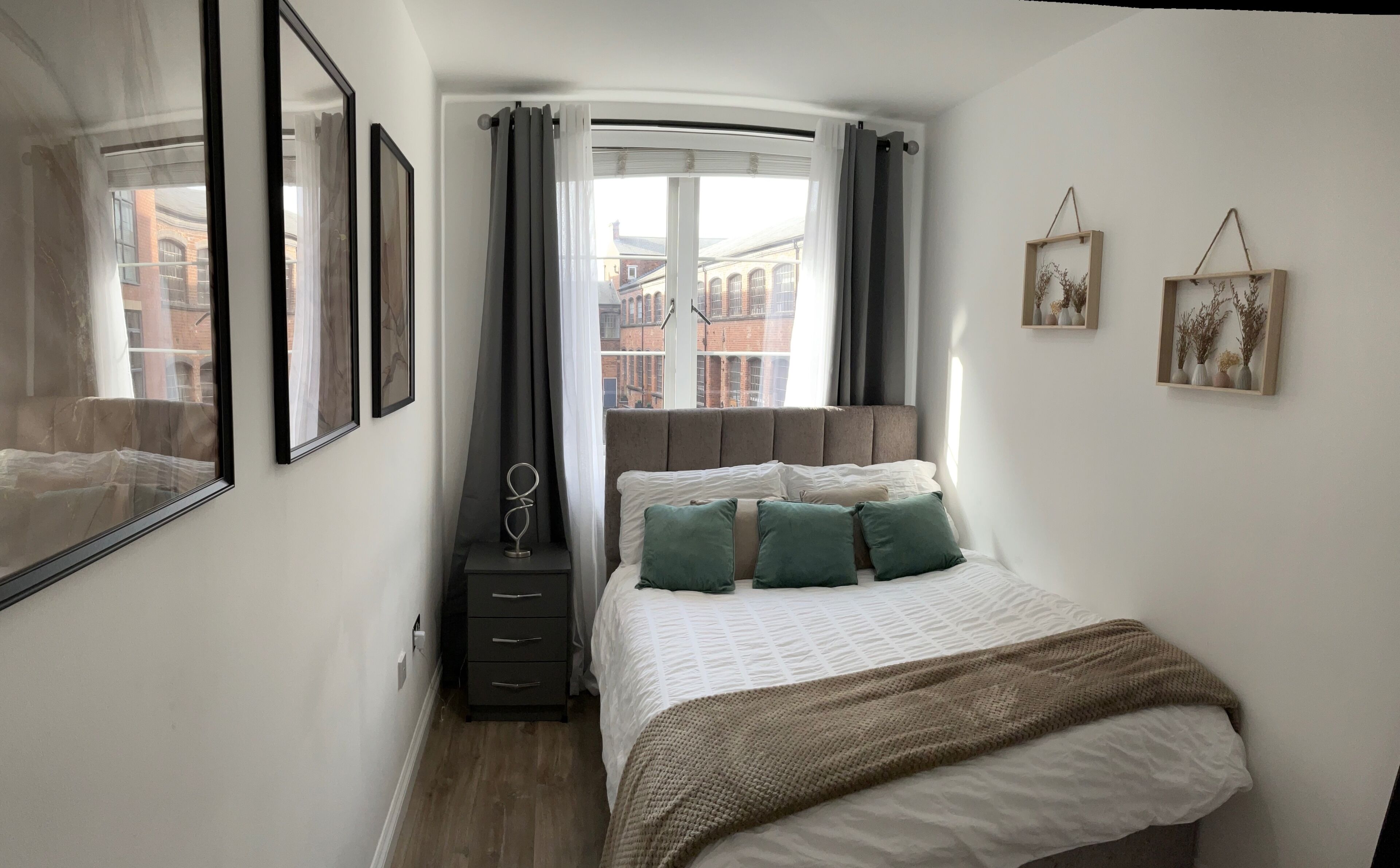 Una camera da letto con un letto, una cassettiera, una finestra con tende e quadri appesi al muro.