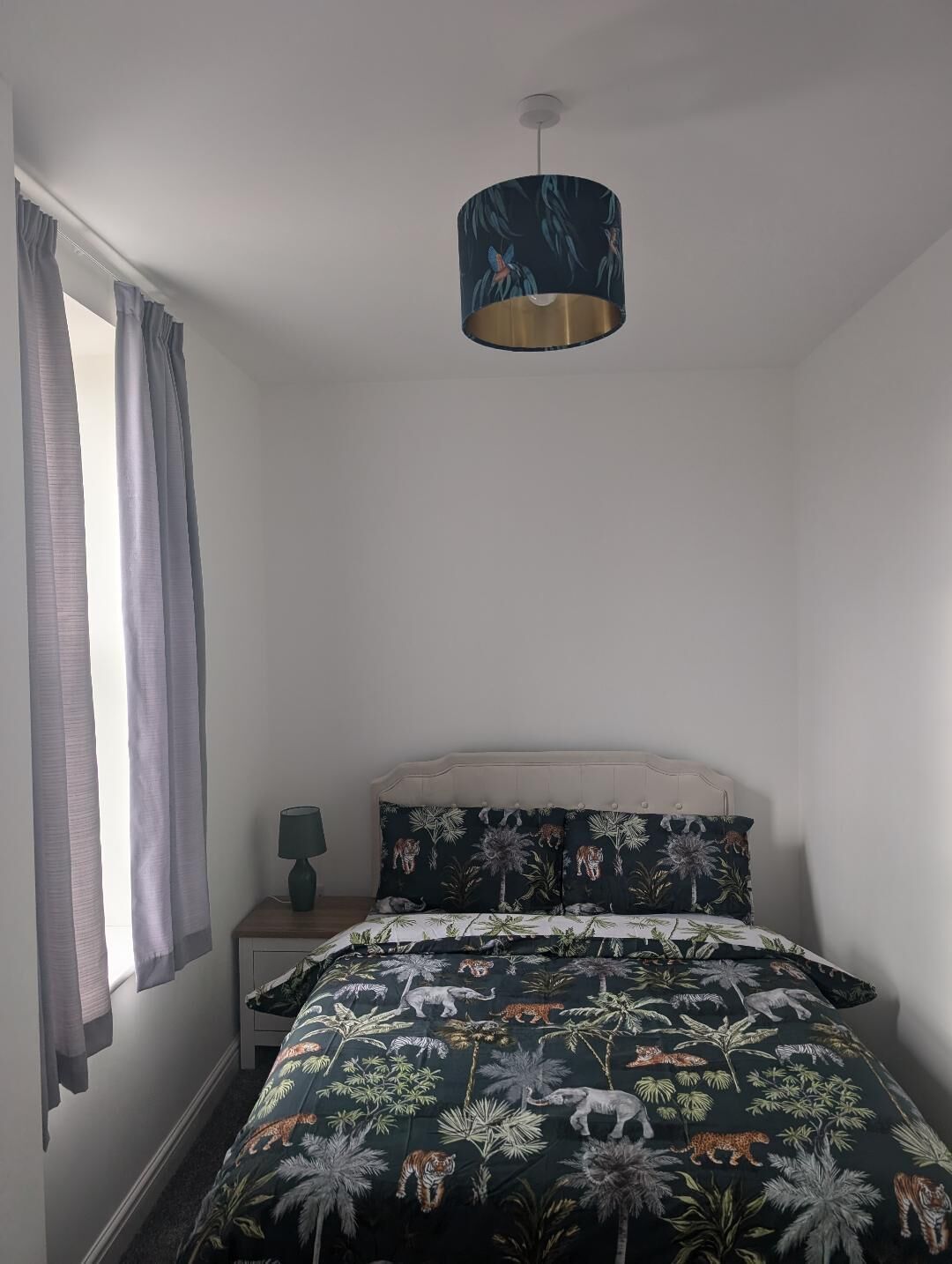 Ein Schlafzimmer mit einem Bett, einem Nachttisch, einer Lampe und einem Fenster mit Vorhängen.