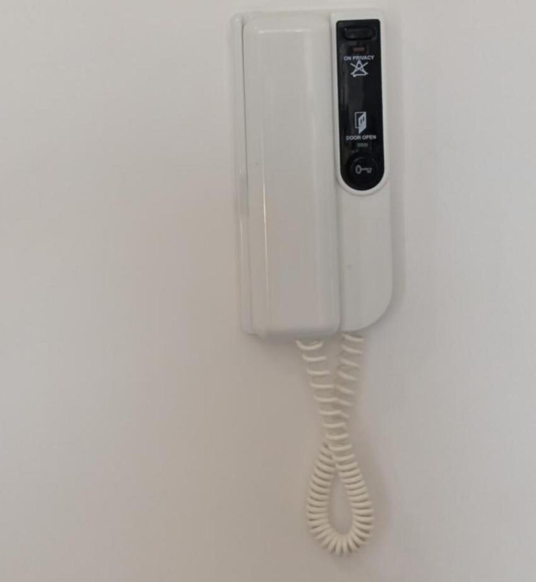 A white telephone mounted on a wall with a coiled cord.