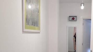 A hallway with a framed abstract painting, a hanging pendant light, and a door at the end.