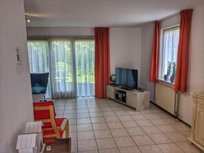 Un soggiorno con televisore, una poltrona, un tavolino e una finestra con tende.