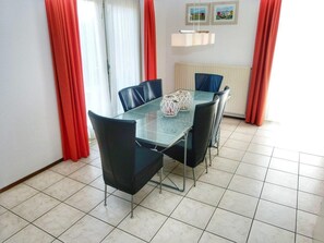 A dining area with a glass table, black chairs, red curtains, and a radiator. - Bungalow in Breskens Near Beach & Lighthouse (Breskens)