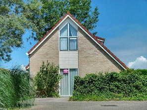 Un edificio a due piani con tetto a punta, un ingresso ben visibile e un cartello sulla porta.