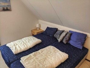 A bedroom with two beds, a nightstand with a lamp, and a painting on the wall. - Bungalow in Breskens Near Beach & Lighthouse (Breskens)