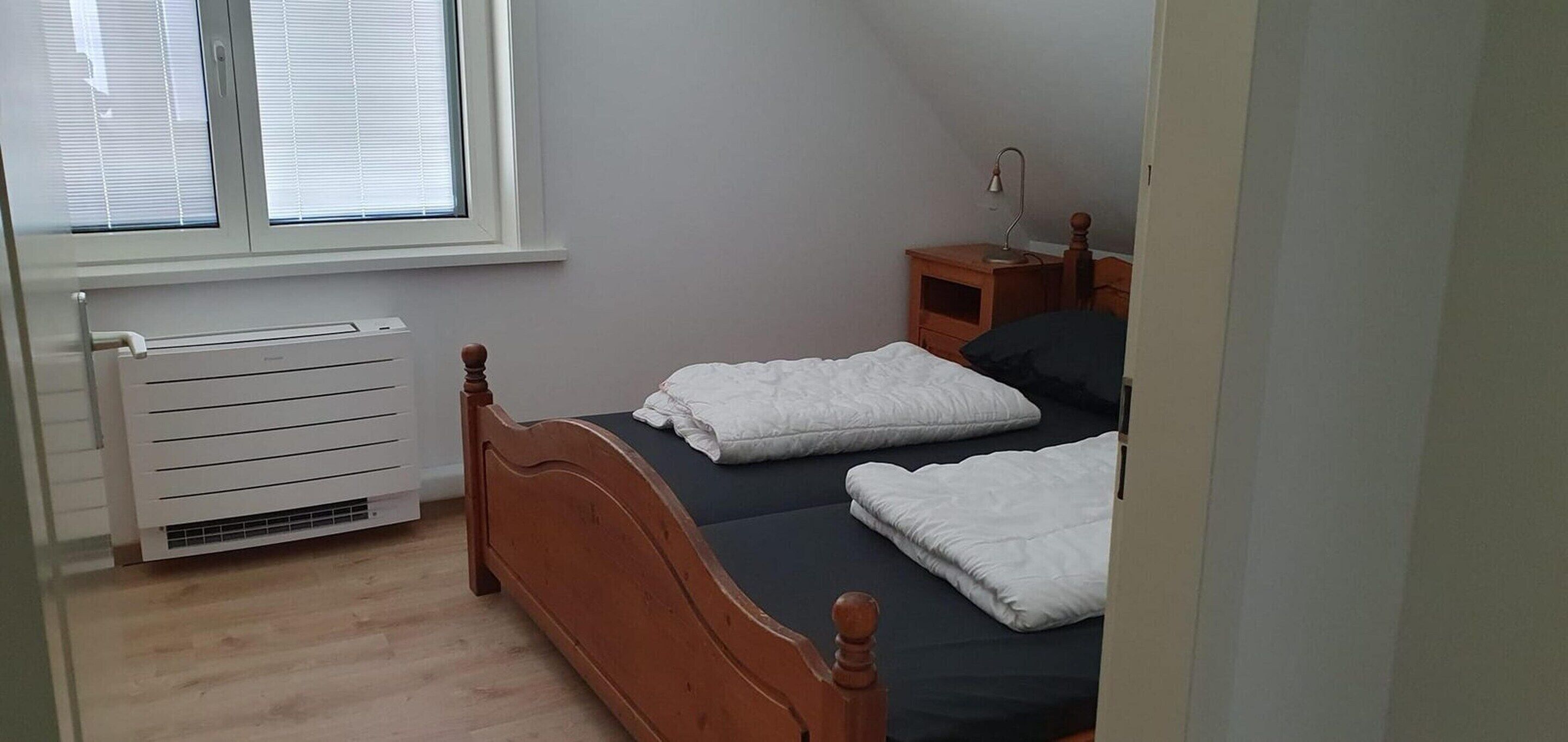 Une chambre  à coucher avec un lit, une table de chevet, une lampe et une fenêtre avec des stores.