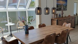 A dining area with a wooden table and chairs, a vase with flowers, and pendant lights. - Eco-friendly Holiday Home (Breskens)