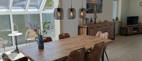 A dining area with a wooden table and chairs, a vase with flowers, and pendant lights.