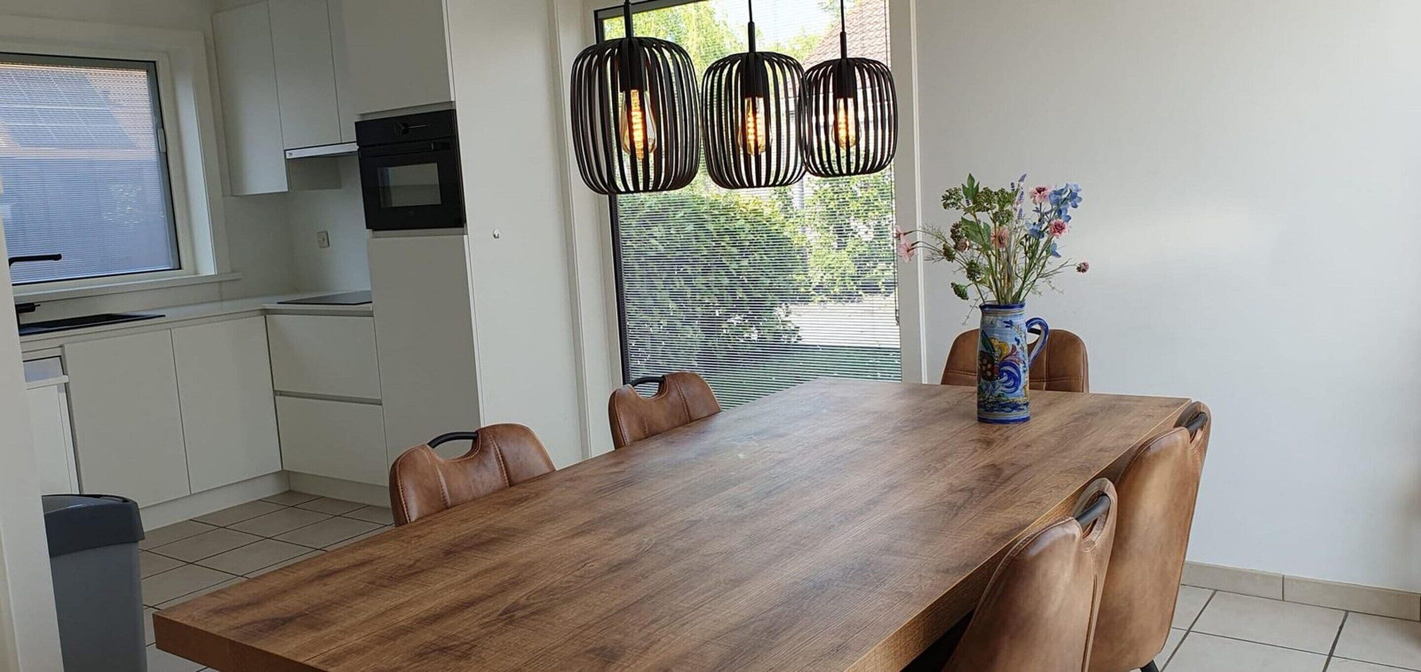 Une cuisine moderne avec des meubles blancs, une table à manger en bois et un vase rempli de fleurs.
