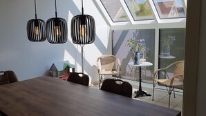 A dining area with a wooden table and chairs, a small decorative house, and a window with a view of a garden. - Eco-friendly Holiday Home (Breskens)