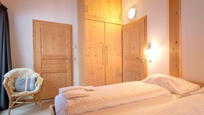 A bedroom with two beds, wooden wardrobes, a wicker chair, and a wall-mounted light. - Beautiful Chalet With hot tub (Stadl-Predlitz)