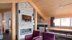 A modern living room with a stone fireplace, wooden beams, and a dining area with purple chairs. - Beautiful Chalet With hot tub (Stadl-Predlitz)
