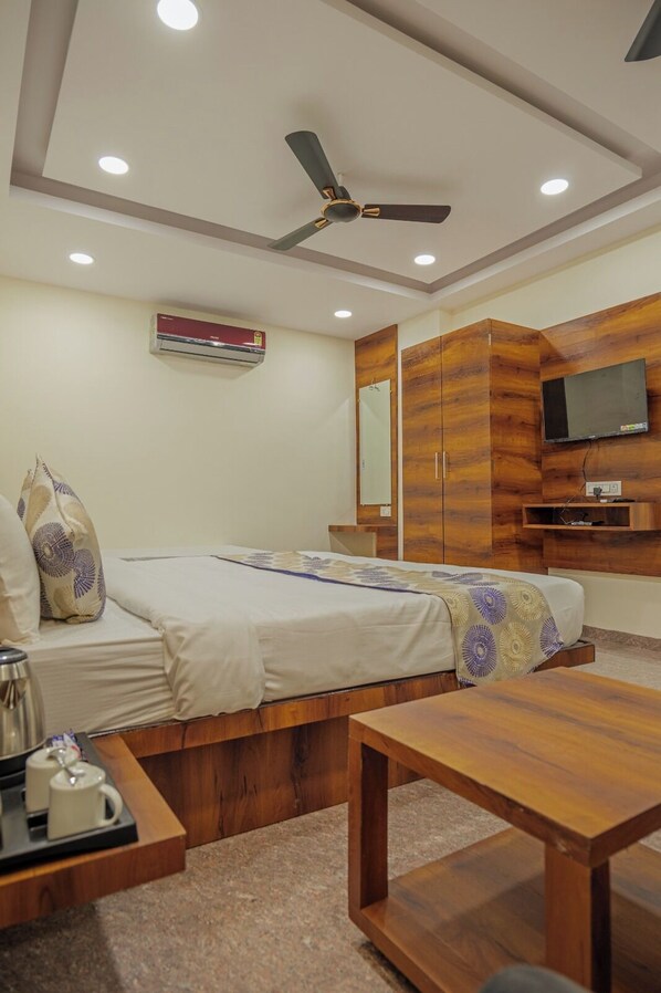 A hotel room with a bed, a wooden table, a TV, and a ceiling fan. - Hotel Dream Inn (Sanwer)