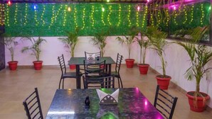A restaurant with tables and chairs, potted plants, and string lights on the ceiling. - Hotel Dream Inn (Sanwer)