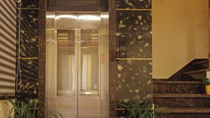 An elevator with a digital display, flanked by potted plants, in a lobby with a marble floor and a Buddha statue. - Hotel Dream Inn (Sanwer)