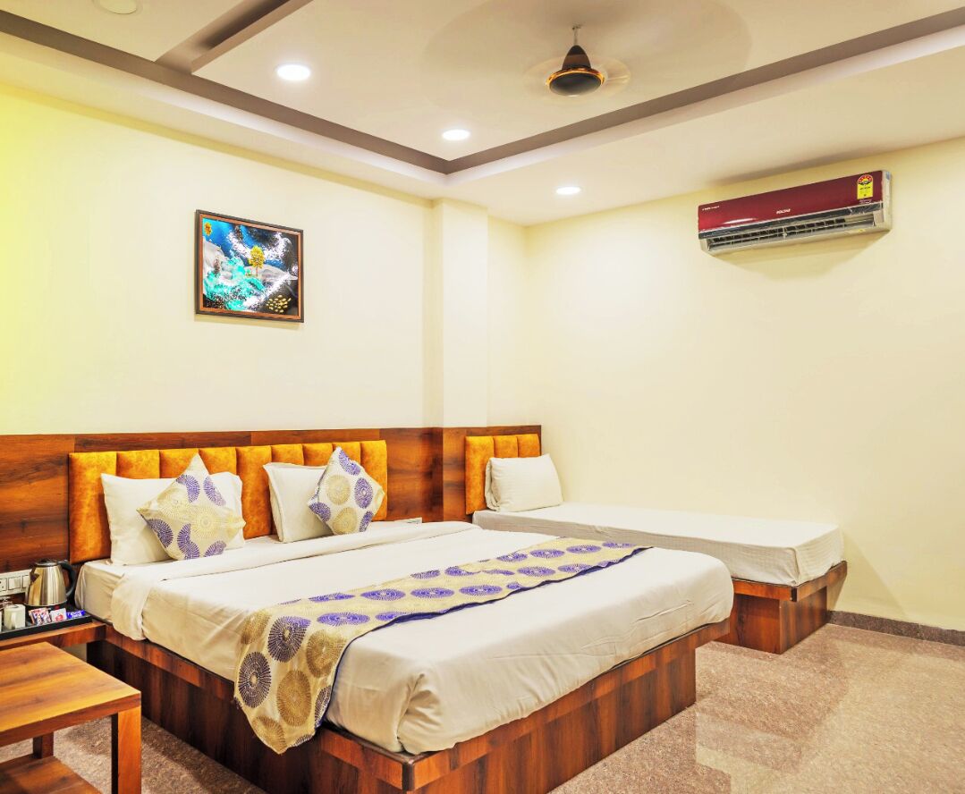 A hotel room with a wooden headboard, a bed with a patterned bedspread, a bedside table with a lamp, and an air conditioning unit on the wall.