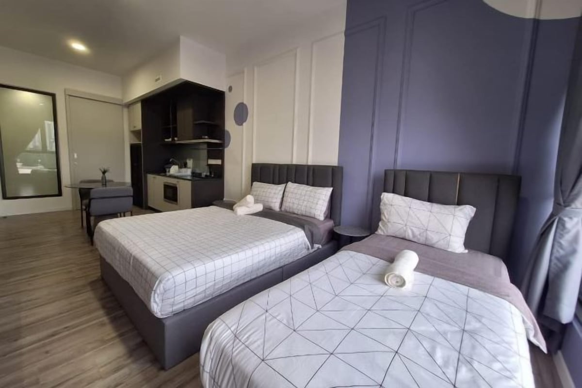 Quarto de hotel com duas camas, uma kitchenette pequena e um espaço de estar.