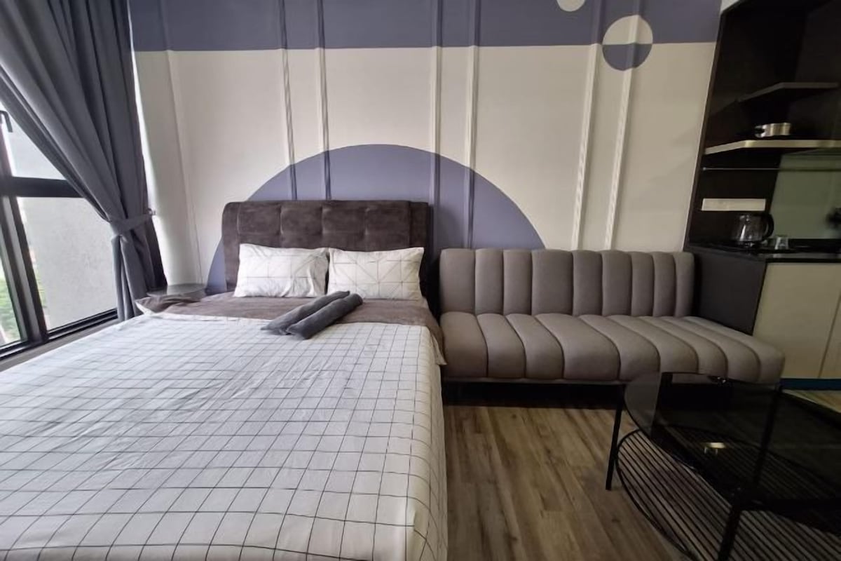 Quarto com cama, sofá, uma mesinha e cozinha equipada com fogão.