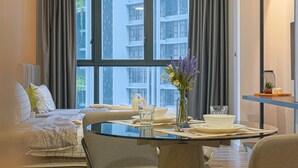 Een moderne hotelkamer met een zithoek, een bed met uitzicht op de stad, en een tafeltje met een bloevas.
