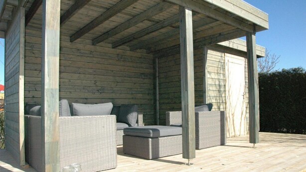 Un espacio de estar al aire libre techado, con mobiliario de mimbre y una terraza de madera.