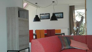 Una sala moderna con un sofá rojo, un aparador de madera y un comedor con sillas color naranja.