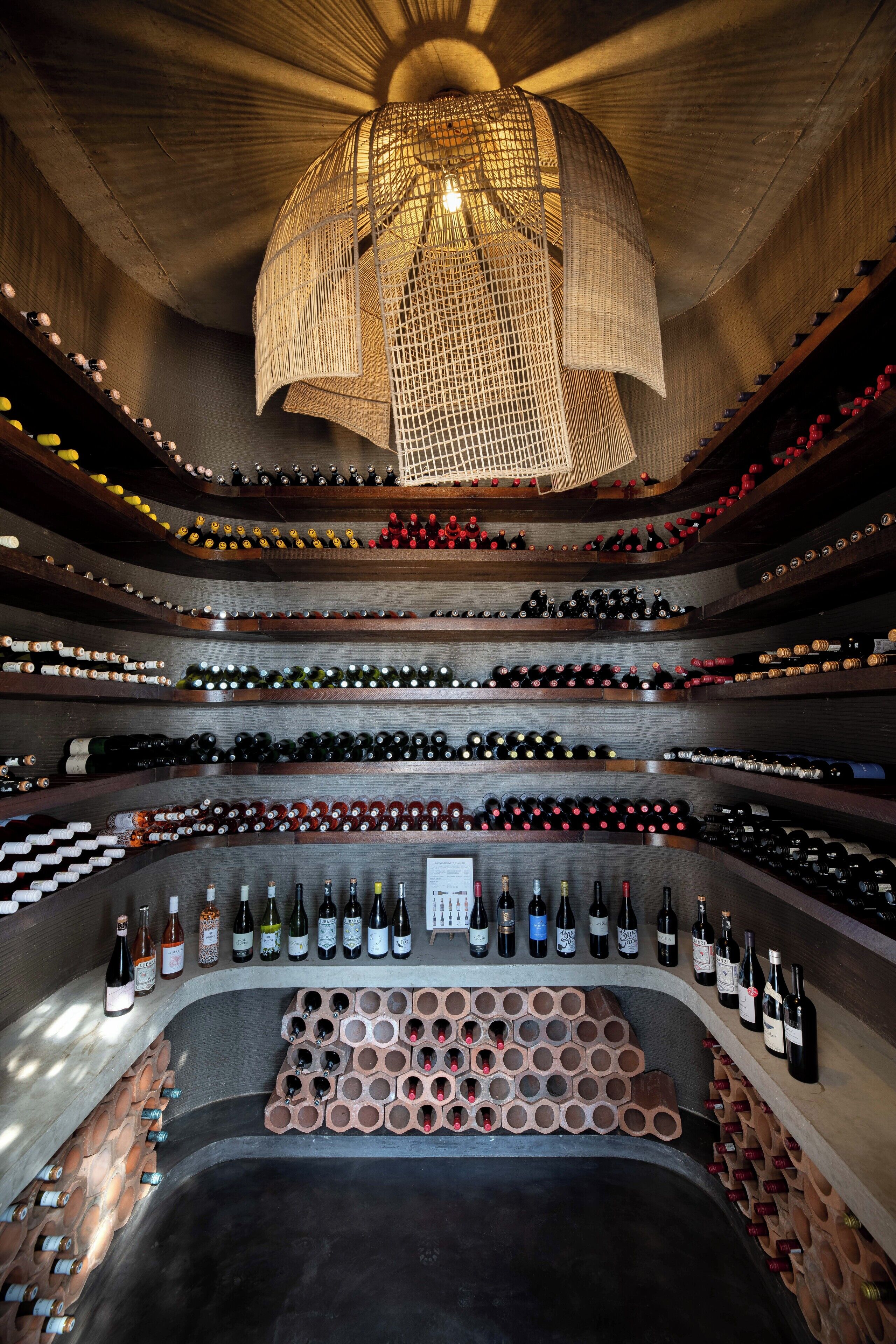 A wine cellar with multiple shelves of wine bottles, a central wine rack, and a hanging light fixture.