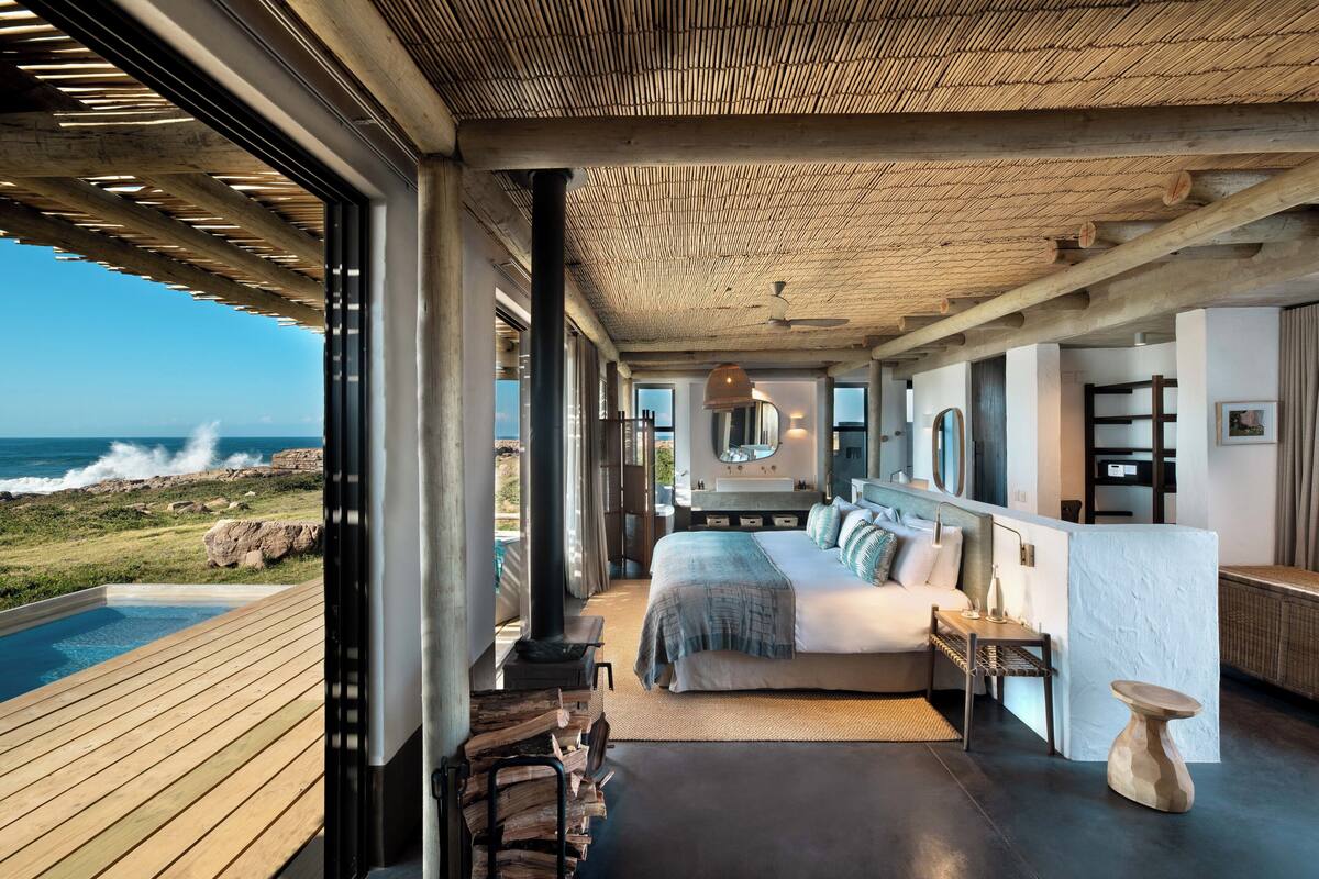 Ein Schlafzimmer mit einem großen Bett, Meerblick, einer Holzterrasse und einem Steinkamin.