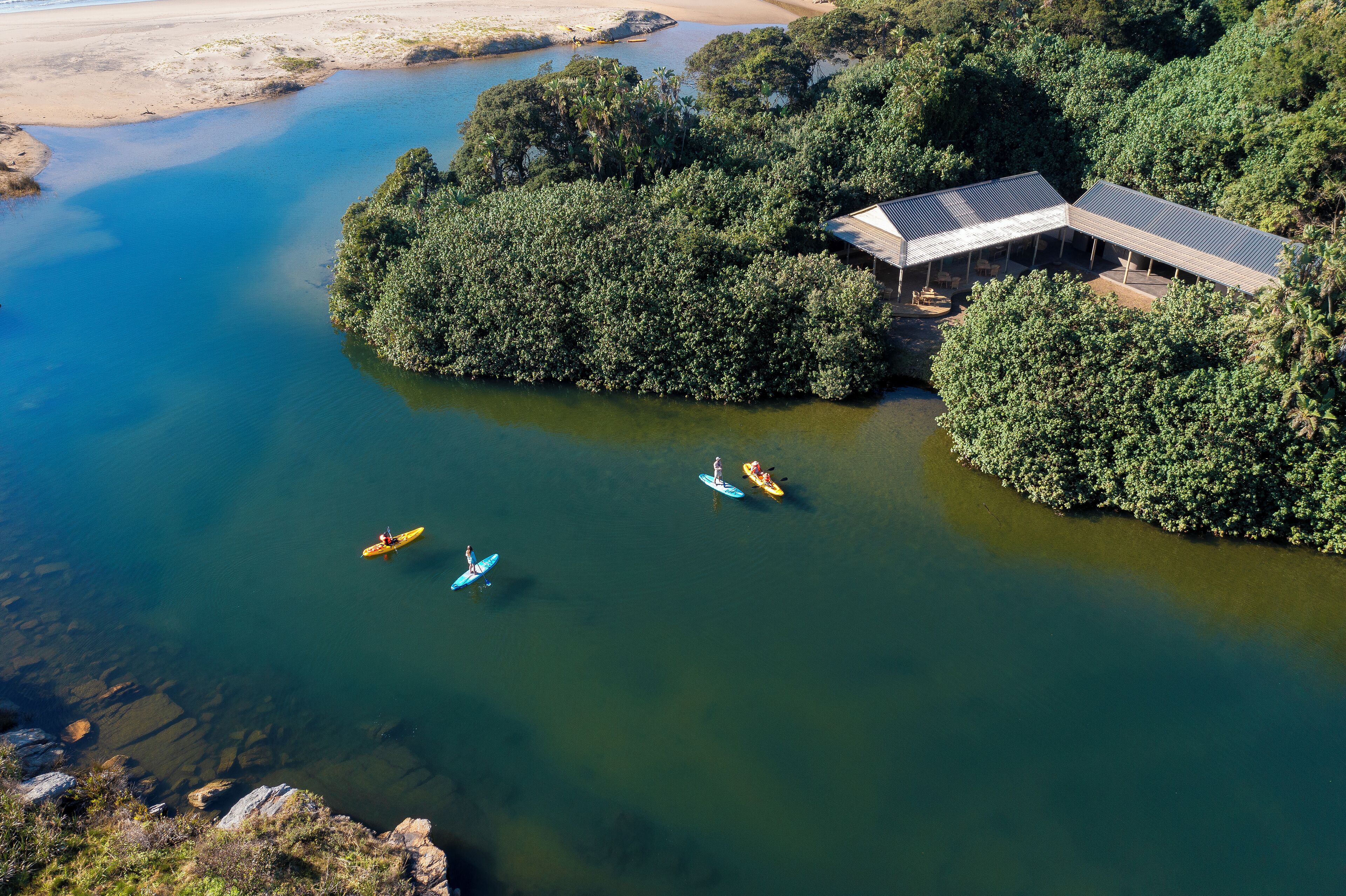 An aerial view of a riverside property with a building and kayaks on the water.