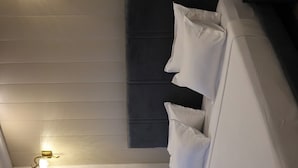 A modern bedroom with a white headboard, a wall-mounted light fixture, and a dark-colored headboard panel.