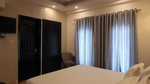 A hotel room with a bed, a chair, a wardrobe, and a television on the wall.