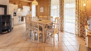 A wooden interior with a dining table, chairs, a kitchen area, and large windows with curtains. - Traditional Chalet With Terrace (Sankt Georgen am Kreischberg)