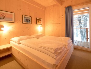 Ein Zimmer mit Holzboden, einem Bett, zwei Wandlampen und einem Fenster mit Blick auf schneebedeckte Bäume.