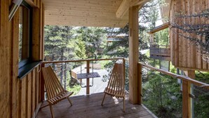 A wooden deck with two wooden chairs and a table, overlooking a forested area. - Chalet in Austria Near Ski Slopes & Sauna (Stadl-Predlitz)