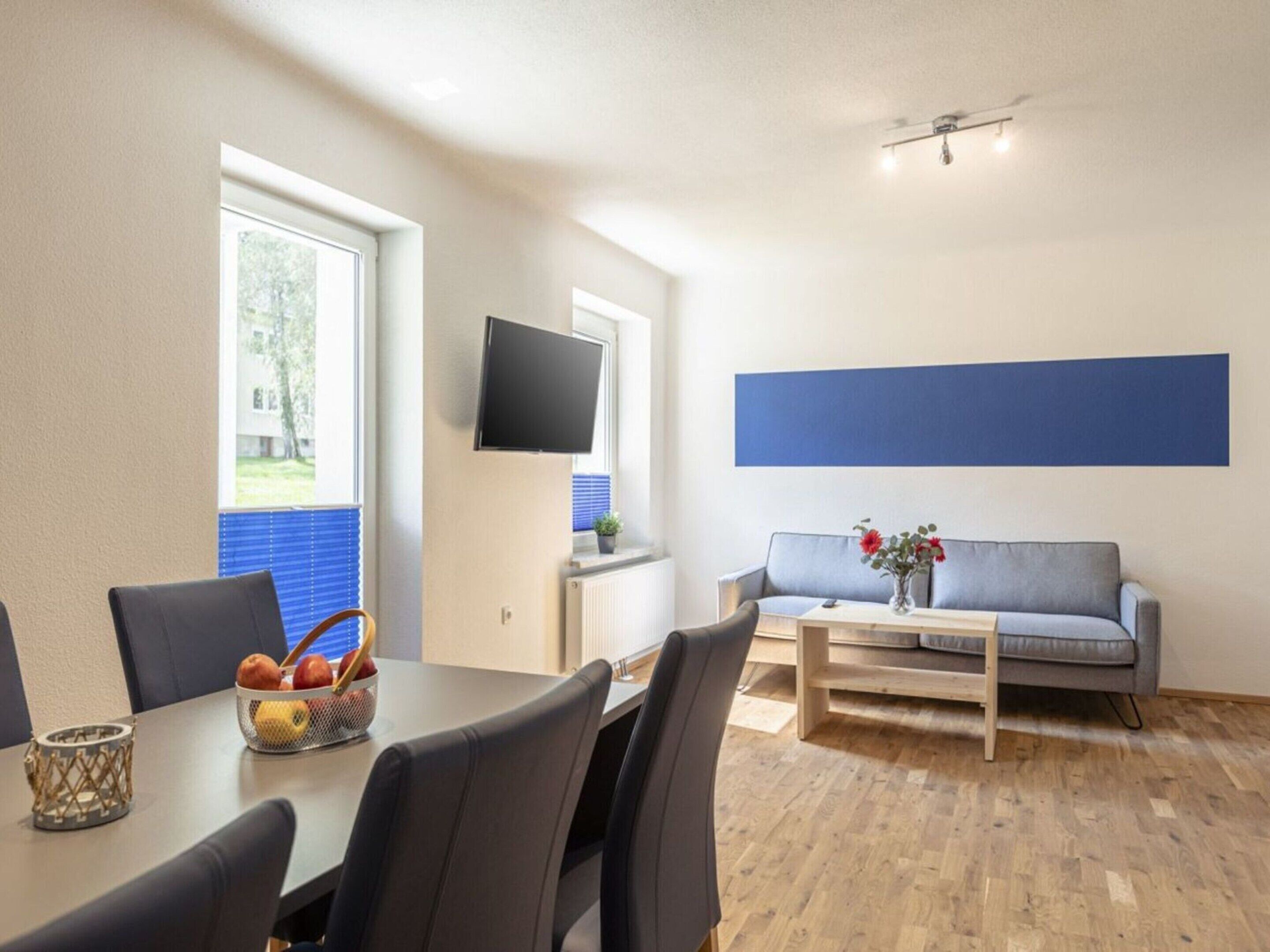 Una sala de estar moderna con una mesa de comedor, sillas, un sofá, un televisor y una ventana con persianas.