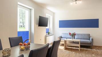Una sala de estar moderna con una mesa de comedor, sillas, un sofá, un televisor y una ventana con persianas.