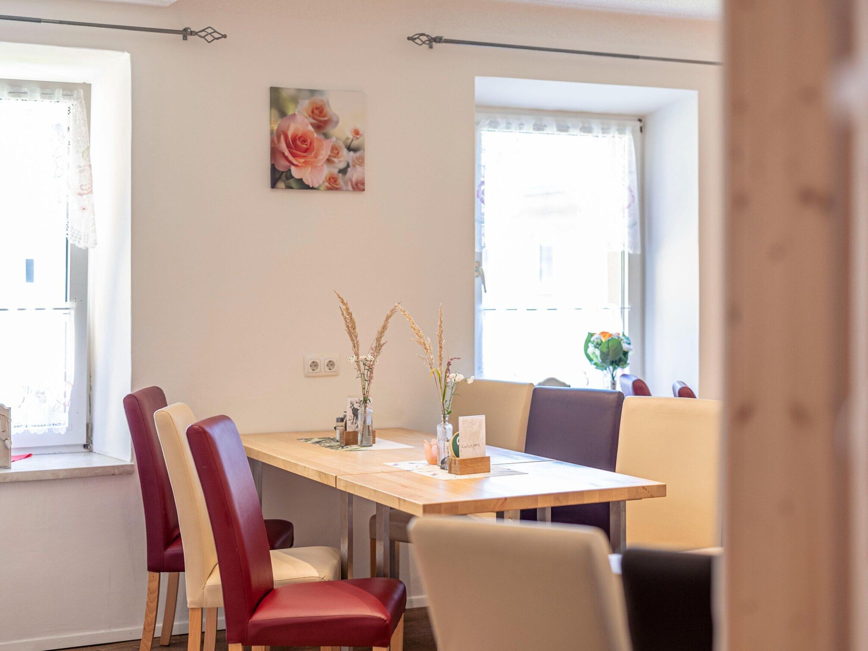 Een eetgedeelte met een houten tafel, rode en beige stoelen, en een vaas met gedroogde planten.