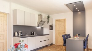Een moderne keuken met witte kastjes, een inbouwoven en een eethoek met een tafel en stoelen.