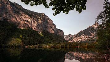 A mountain landscape with a clear lake reflecting the surrounding cliffs and trees.