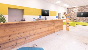 Een receptiegedeelte met een houten balie, een stenen muur en een kleurenschema in geel en wit.
