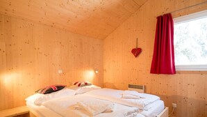 A wooden cabin bedroom with a bed, pillows, a heater, and a window with red curtains. - Chalet in Turracher Hohe Near Ski Slopes (Stadl-Predlitz)