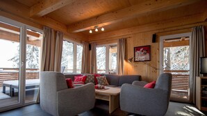 A cozy cabin interior with a wooden ceiling, large windows, a sofa with cushions, and a television. - Chalet in Turracher Hohe Near Ski Slopes (Stadl-Predlitz)