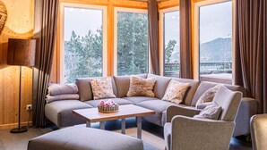 A cozy living room with a sectional sofa, a small table, and a view of a forest and mountains through large windows. - Chalet in Austria Near Ski Slope & Sauna (Stadl-Predlitz)