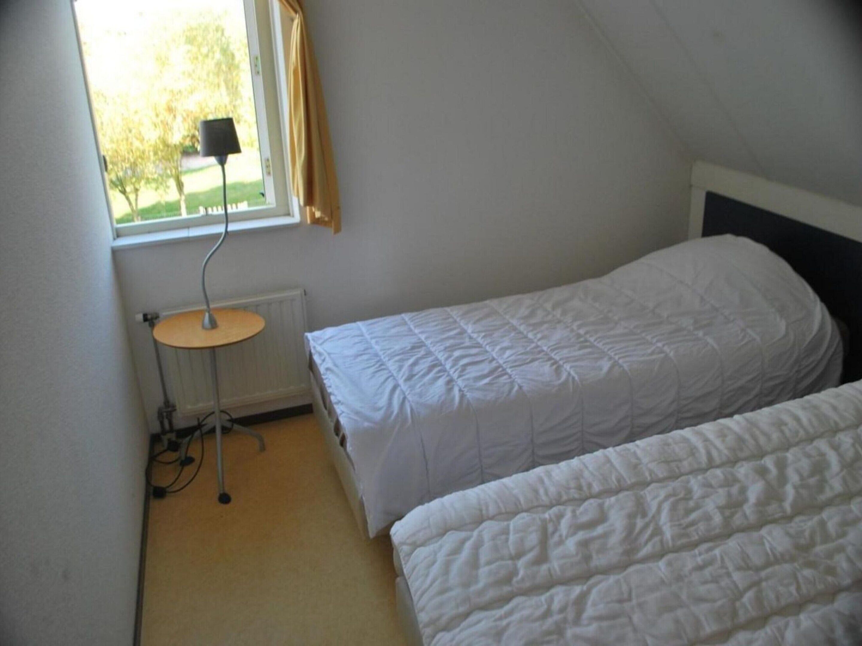 Pequeña habitación individual con dos camas, un escritorio y una ventana con cortinas.
