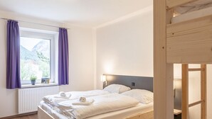 A bedroom with a wooden bed, a window with purple curtains, a radiator, and a view of mountains. - Modern Apartment With Balcony (Eisenerz)