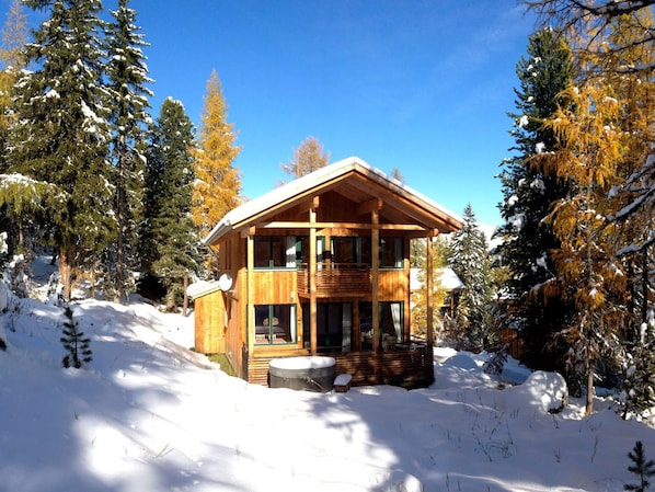 A wooden cabin with a balcony, surrounded by snow-covered trees.