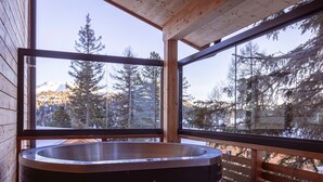 Un bain à remous dans un chalet en bois doté de grandes fenêtres donnant sur une zone boisée.